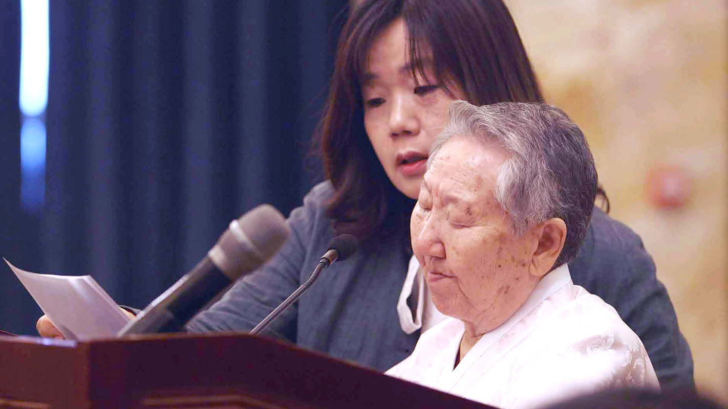 Gil Won-Ok reading her speech in China, supported by a Cao Hei Mao and her daughter activist Meehyang Yoon.
