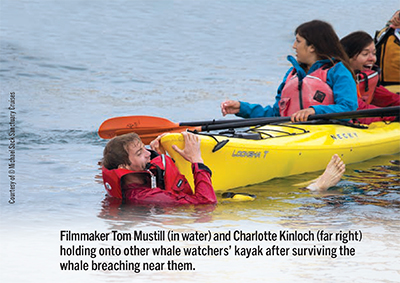 Filmmaker Tom Mustill (in water) and Charlotte Kinloch (far right) holding onto other whale watchers’ kayak after surviving the whale breaching near them.