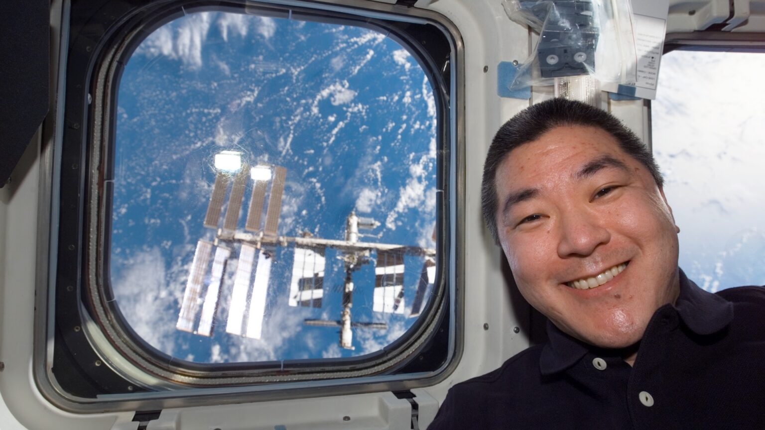 S122-E-010906 (18 Feb. 2008) --- Astronaut Daniel Tani, STS-122 mission specialist, poses for a photo near a window on the aft flight deck of Space Shuttle Atlantis shortly after undocking from the International Space Station, which is visible through the window.